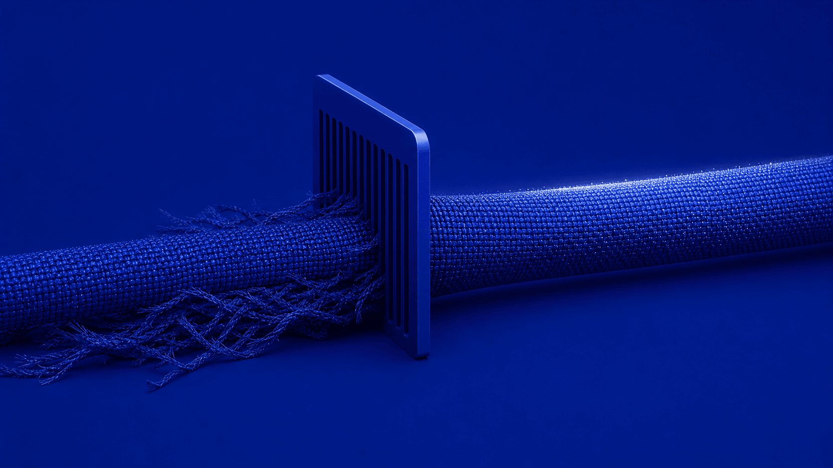 A sculptural comb filters a continuous ultramarine carrier while a controlled fringe of fibers remains behind.